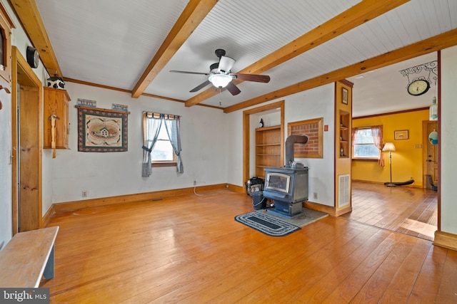 unfurnished living room featuring beam ceiling, a wood stove, ceiling fan, and light wood-type flooring