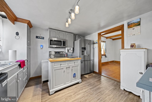 kitchen featuring wooden counters, light hardwood / wood-style flooring, gray cabinets, ornamental molding, and stainless steel appliances