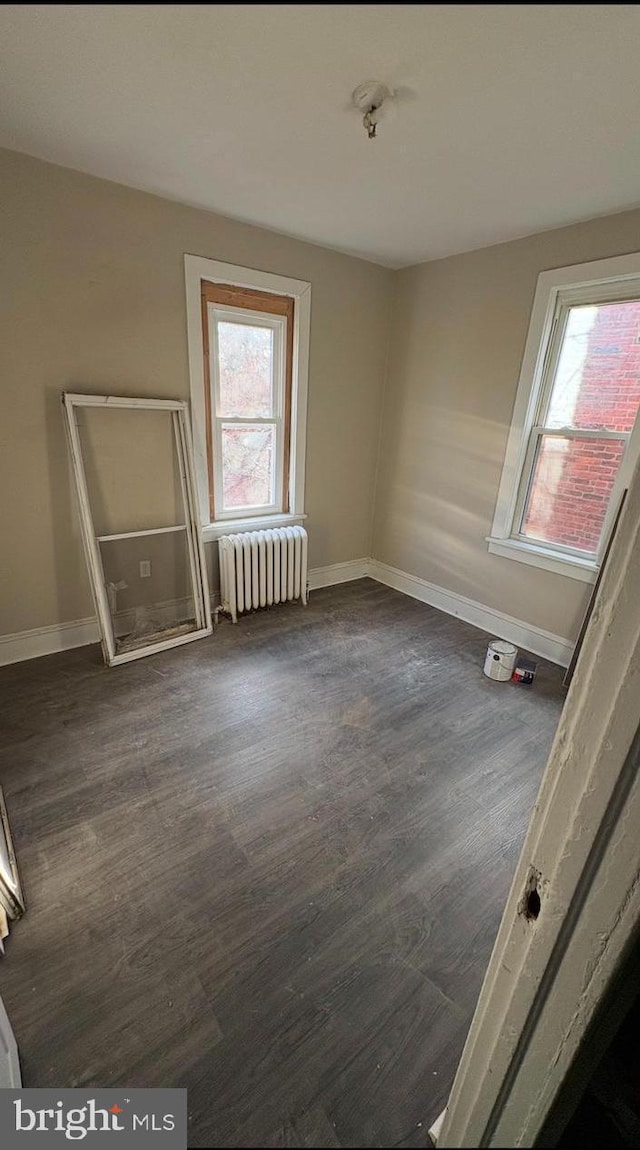 spare room featuring a healthy amount of sunlight, radiator heating unit, and dark hardwood / wood-style floors