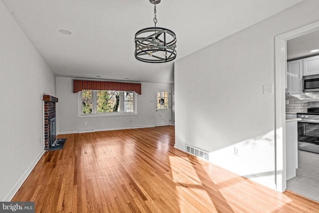 unfurnished living room featuring a notable chandelier, light hardwood / wood-style floors, and a brick fireplace