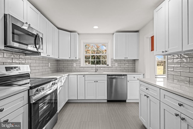 kitchen with white cabinetry, sink, light stone counters, decorative backsplash, and appliances with stainless steel finishes