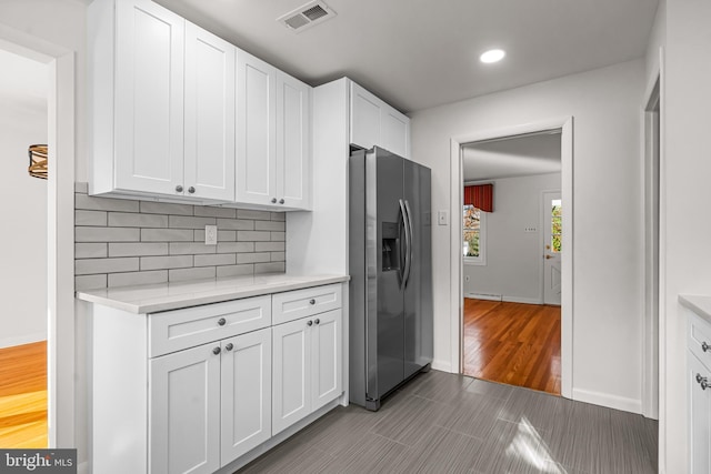 kitchen featuring stainless steel fridge, backsplash, and white cabinetry