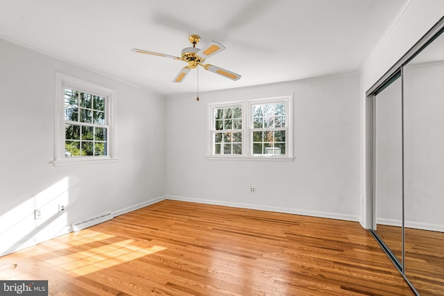 unfurnished bedroom with ceiling fan, baseboard heating, light hardwood / wood-style flooring, crown molding, and a closet