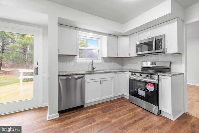 kitchen with light stone countertops, appliances with stainless steel finishes, dark wood-type flooring, sink, and white cabinets