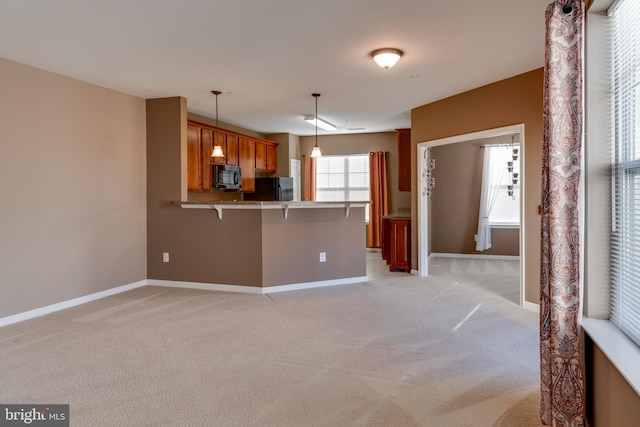 kitchen featuring light carpet, a breakfast bar area, black appliances, kitchen peninsula, and pendant lighting