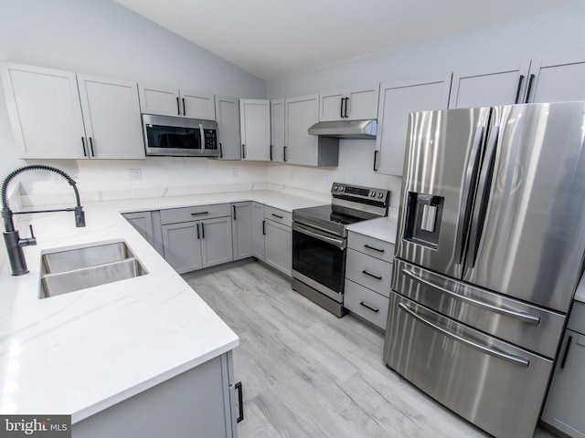 kitchen with lofted ceiling, gray cabinetry, appliances with stainless steel finishes, a sink, and under cabinet range hood