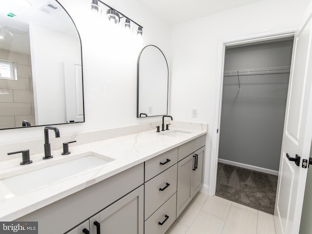 bathroom with double vanity, visible vents, a walk in closet, and a sink