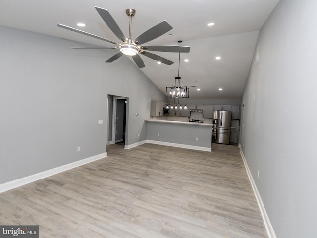 unfurnished living room featuring ceiling fan with notable chandelier, high vaulted ceiling, light wood finished floors, and baseboards