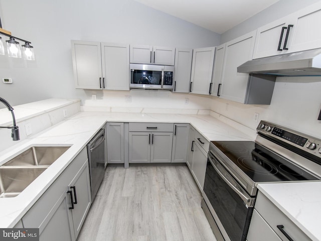 kitchen with lofted ceiling, appliances with stainless steel finishes, gray cabinets, under cabinet range hood, and a sink