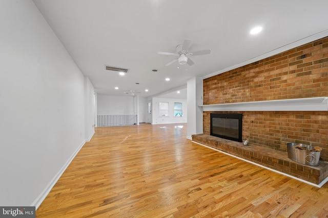 unfurnished living room featuring light wood-type flooring, a brick fireplace, and ceiling fan