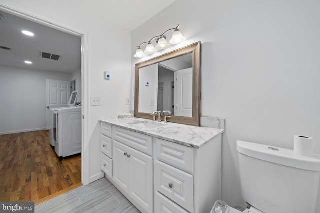 bathroom with toilet, wood-type flooring, separate washer and dryer, and vanity