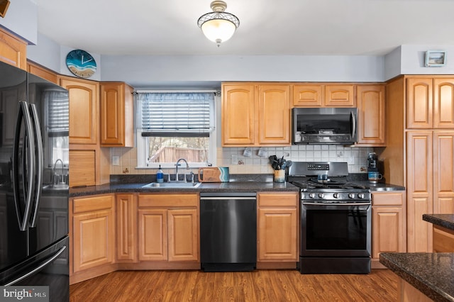 kitchen with backsplash, dark stone counters, sink, black appliances, and light hardwood / wood-style flooring