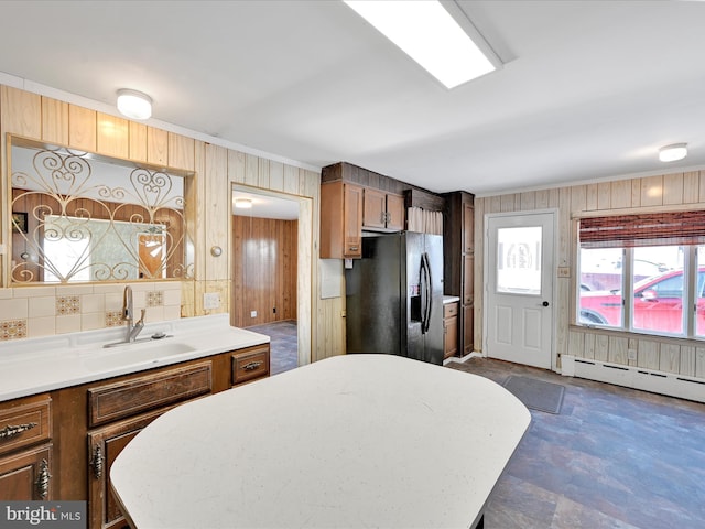 kitchen with black fridge with ice dispenser, sink, wooden walls, and a baseboard heating unit