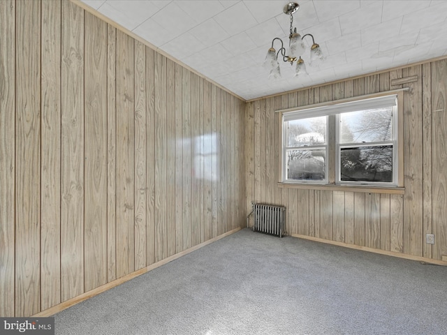 unfurnished room featuring radiator, light carpet, wooden walls, and a chandelier