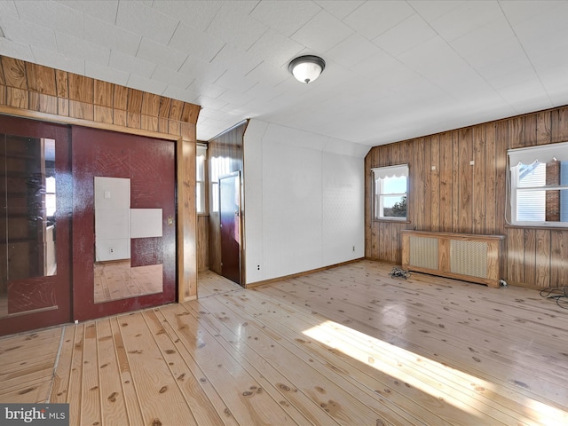 interior space with light hardwood / wood-style flooring, radiator, and wood walls