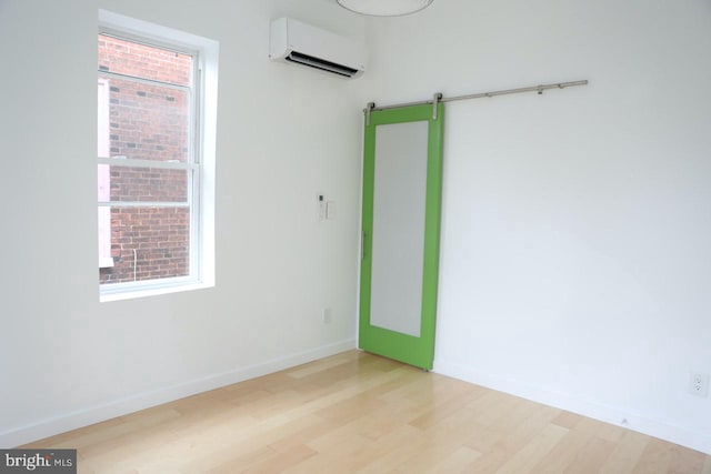 empty room with an AC wall unit, a barn door, and light hardwood / wood-style floors