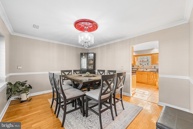 dining space with an inviting chandelier, ornamental molding, and light hardwood / wood-style floors