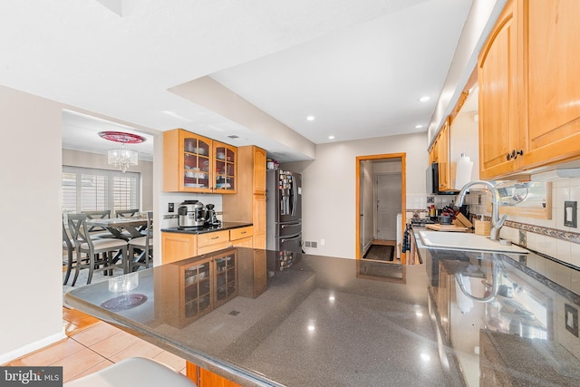 kitchen with kitchen peninsula, black fridge, decorative backsplash, sink, and an inviting chandelier