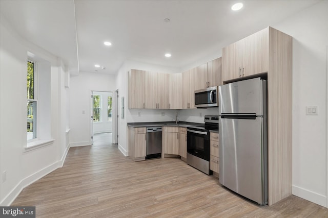 kitchen with light brown cabinets, sink, appliances with stainless steel finishes, and light hardwood / wood-style flooring