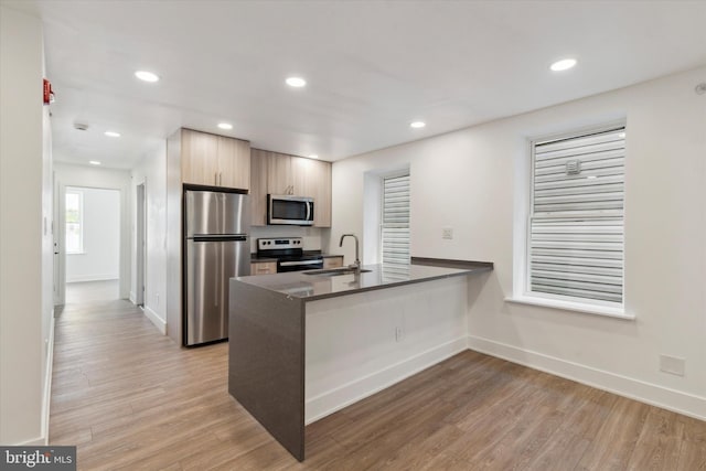 kitchen featuring kitchen peninsula, appliances with stainless steel finishes, light hardwood / wood-style flooring, and sink