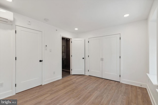 unfurnished bedroom featuring a wall mounted air conditioner and light hardwood / wood-style floors