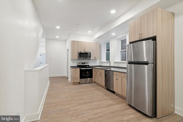 kitchen with light brown cabinets, sink, stainless steel appliances, and light hardwood / wood-style flooring