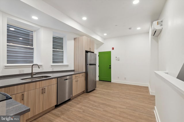 kitchen featuring light brown cabinetry, stainless steel appliances, a wall unit AC, sink, and light hardwood / wood-style floors