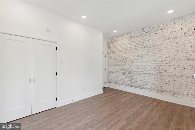 unfurnished bedroom with wood-type flooring and brick wall