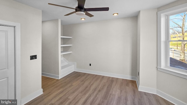 empty room featuring built in features, ceiling fan, and wood-type flooring