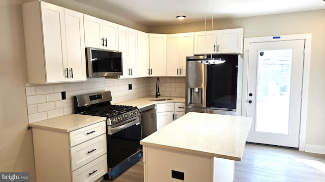 kitchen with stainless steel appliances, white cabinets, a center island, backsplash, and sink