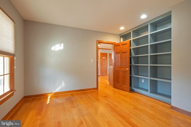 spare room featuring built in shelves and light hardwood / wood-style flooring