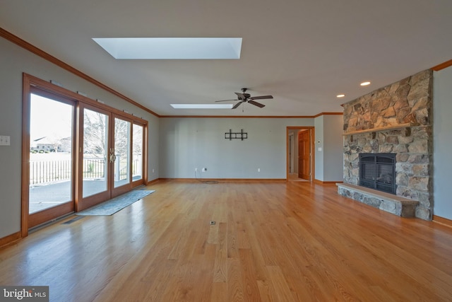 unfurnished living room featuring french doors, a skylight, ceiling fan, light hardwood / wood-style flooring, and a fireplace