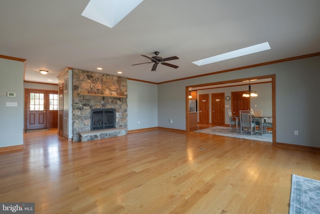 unfurnished living room featuring ceiling fan with notable chandelier, light wood-type flooring, a fireplace, and a skylight