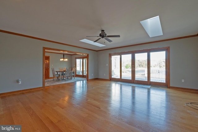 unfurnished living room featuring a skylight, ceiling fan with notable chandelier, light hardwood / wood-style floors, and plenty of natural light