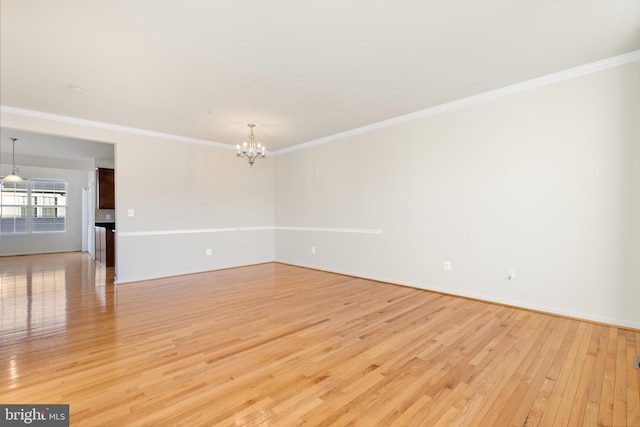 unfurnished room with an inviting chandelier, light wood-type flooring, and crown molding