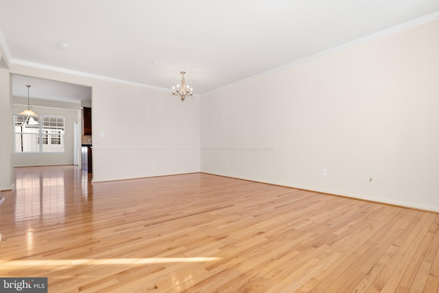 spare room featuring ornamental molding, light wood-type flooring, and an inviting chandelier