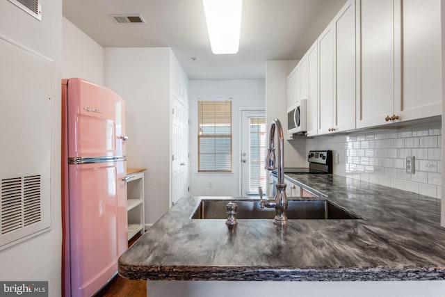 kitchen featuring kitchen peninsula, backsplash, sink, white fridge, and white cabinetry