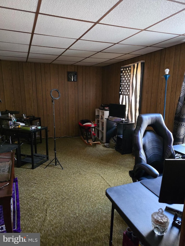 carpeted office featuring a paneled ceiling and wood walls