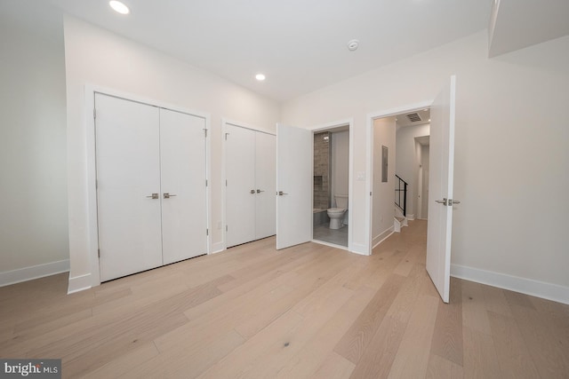 unfurnished bedroom with ensuite bath, two closets, and light hardwood / wood-style flooring