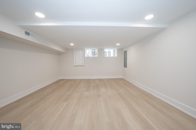 basement featuring electric panel and light hardwood / wood-style flooring