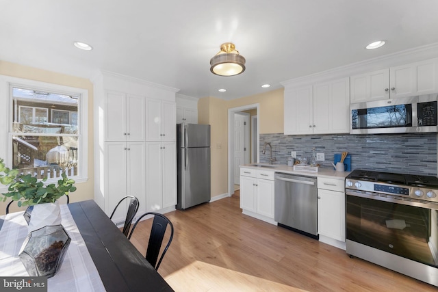 kitchen featuring sink, stainless steel appliances, light hardwood / wood-style flooring, backsplash, and white cabinets