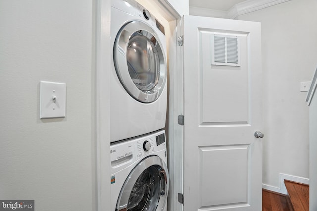 laundry area with stacked washer / drying machine, dark hardwood / wood-style flooring, and ornamental molding