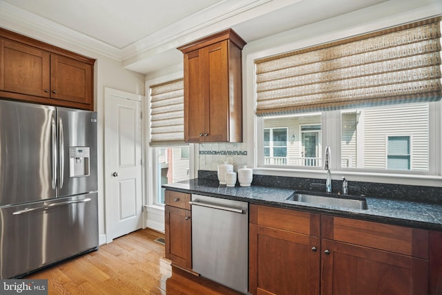 kitchen featuring light wood-type flooring, stainless steel appliances, crown molding, sink, and dark stone countertops