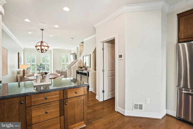 kitchen featuring dark stone counters, crown molding, dark hardwood / wood-style floors, a notable chandelier, and stainless steel refrigerator