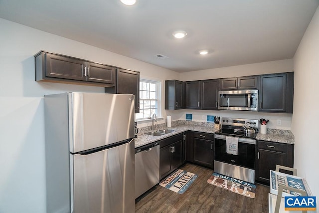 kitchen featuring light stone countertops, appliances with stainless steel finishes, dark wood-type flooring, and sink