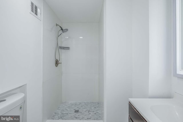 bathroom with toilet, vanity, and tiled shower