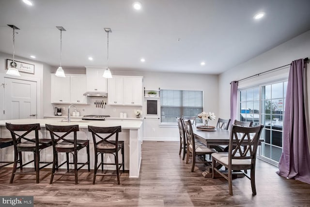 kitchen with a breakfast bar, a kitchen island with sink, hanging light fixtures, dark hardwood / wood-style flooring, and white cabinetry