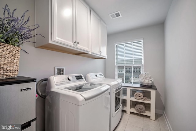 clothes washing area featuring washing machine and dryer, light tile patterned floors, and cabinets