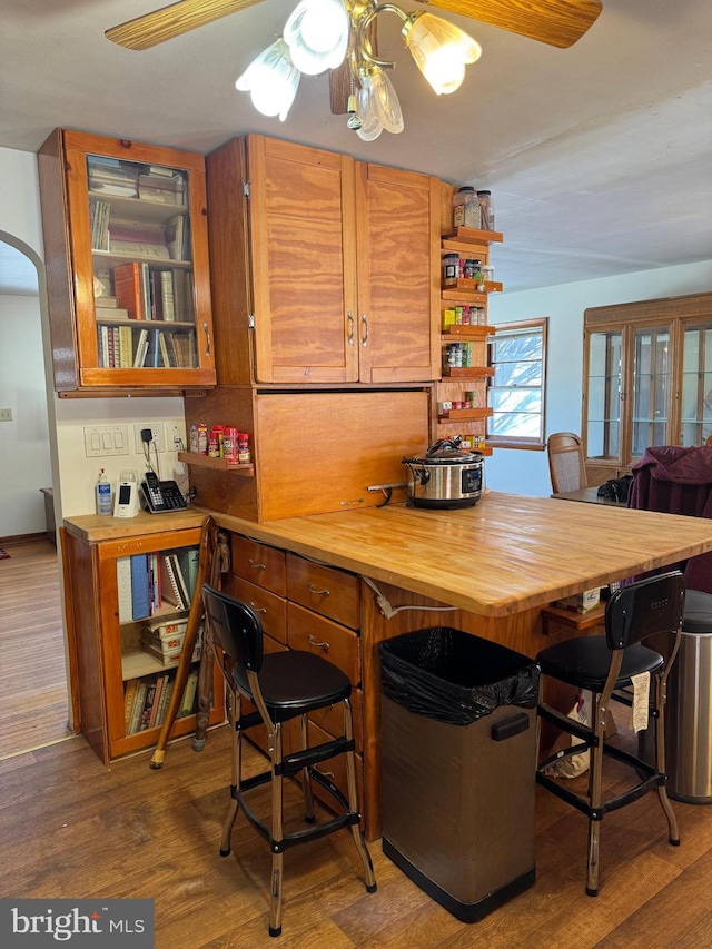 kitchen with butcher block counters, hardwood / wood-style flooring, ceiling fan, and a breakfast bar area