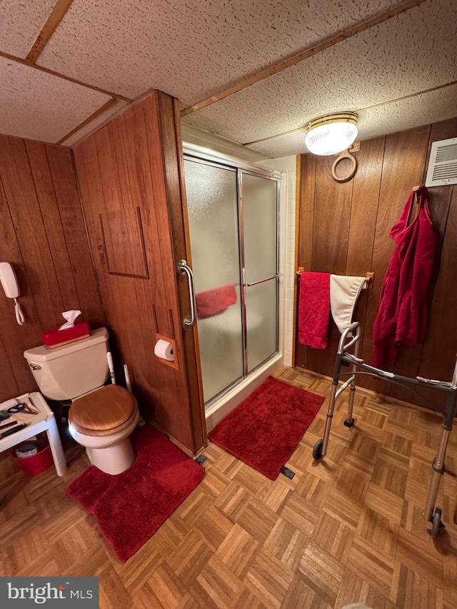 bathroom with wood walls, toilet, a shower with shower door, and parquet floors